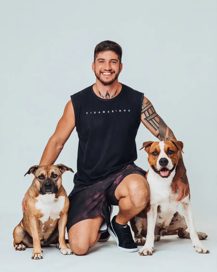 Guilherme Matilha sorrindo, ajoelhado entre dois cães